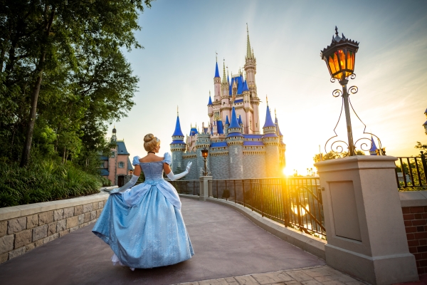 Cinderella in her blue dress stands in front of Cinderella Castle at Magic Kingdom at sunrise.