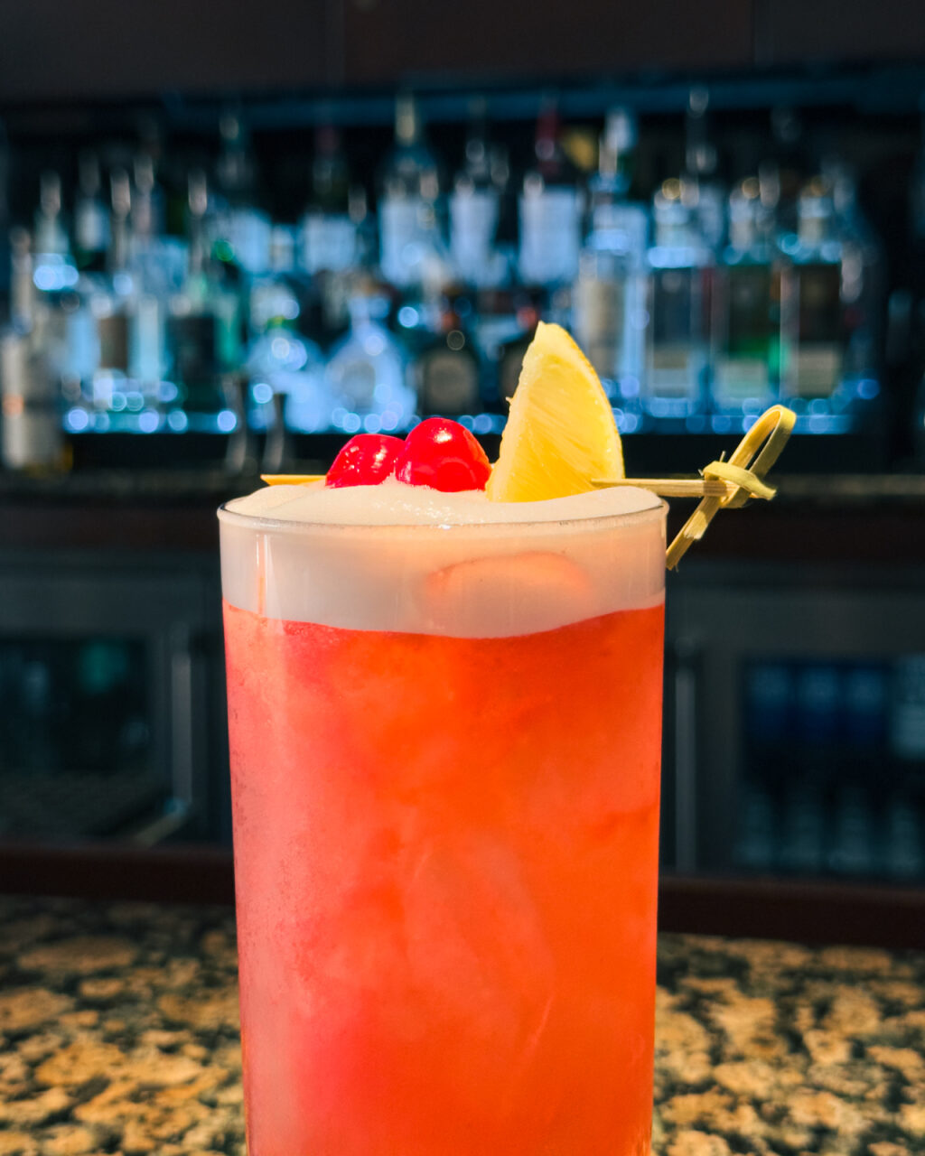 A bright pink cocktail garnished with an orange slice and maraschino cherries. 