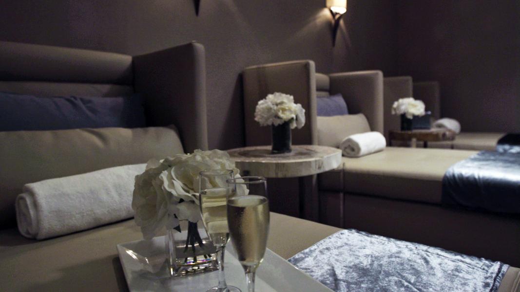 A dimly lit room with rows of neatly made chaise lounges, adorned with flowers and glasses of champagne.