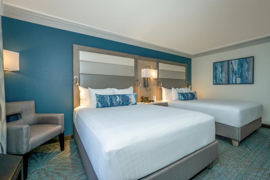 Two queen beds with white linens and a blue throw pillow against a blue painted wall.