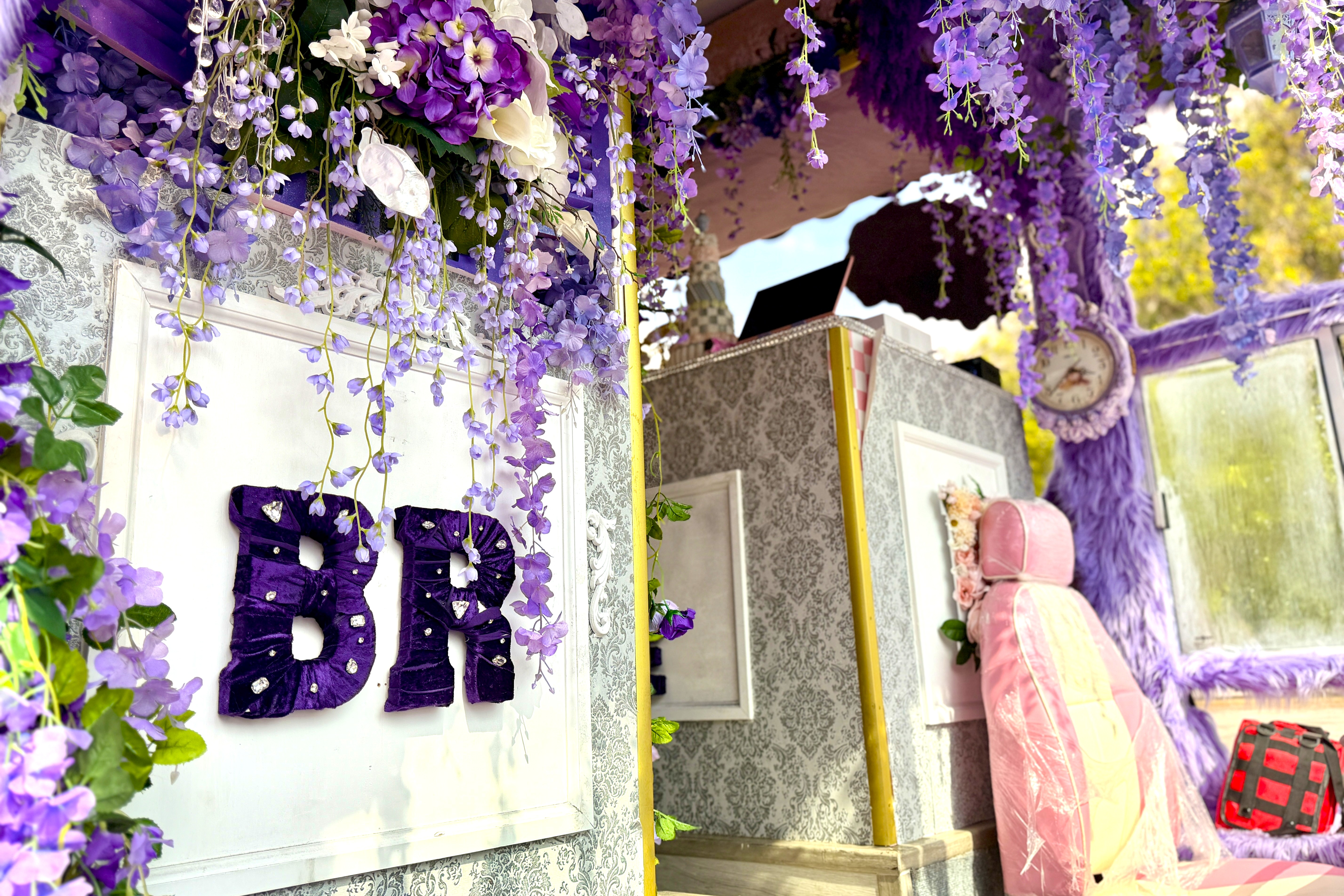 The entrance to a bus decorated with purple letters that say BR and draped purple florals hanging from the ceiling. 