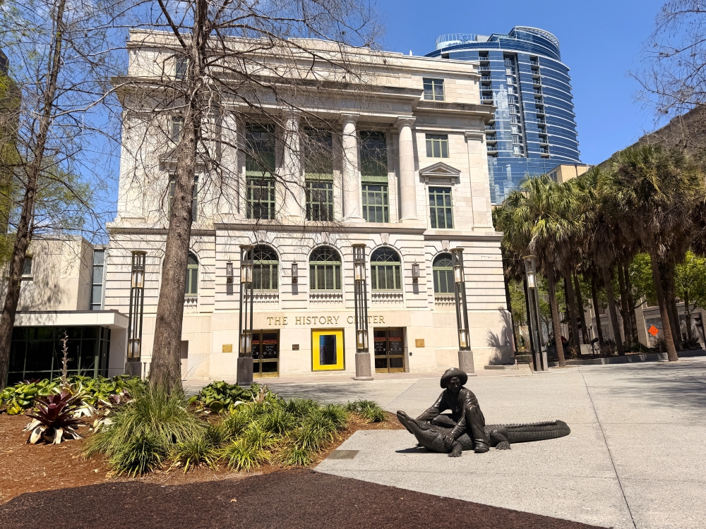 A tall stone building with columns and a statue in front of a man wrangling an alligator.