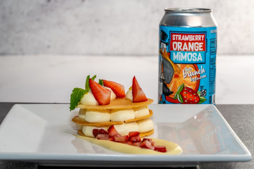 A layered dessert with dollops of cream and strawberries, and a can of beer in the background for Sip & Savor. 