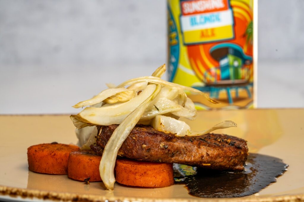 A venison filet on a bed of mole and sweet potato, topped with onions, and a can of beer in the background.