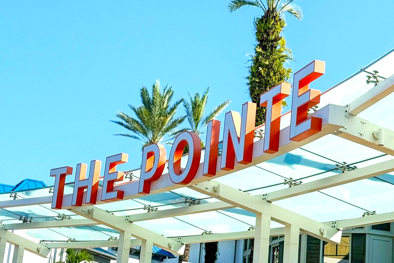 A white and orange sign that reads "The Pointe" with palm trees in the background. 