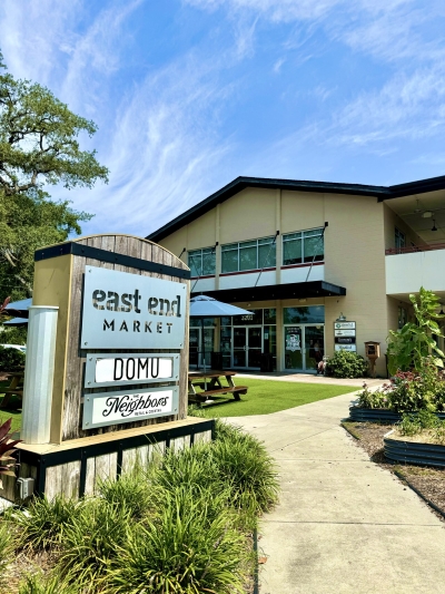 A two-story building with gardens behind a sign that reads East End Market and lists a variety of vendors.