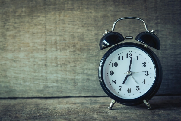 A black classic alarm clock sits against a neutral wooden background.