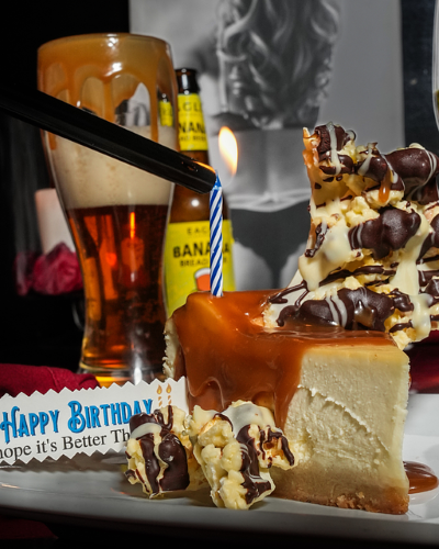 A slice of decadent cheesecake on a plate wiht a glass of wine.