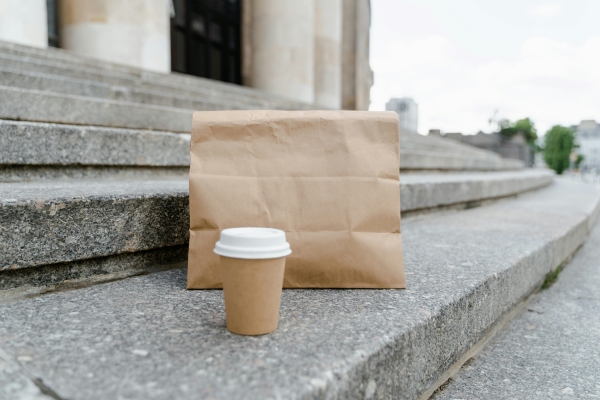 A folded over paper bag and a cup of coffee sit on cement steps.