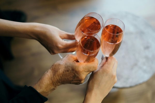 Three hands, including an older woman's, clink Champagne flutes of rose sparkling wine.