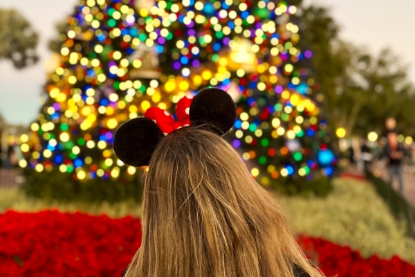 A young woman wearing Minnie Mouse ears faces a glittering Christmas tree during Christmas at EPCOT.