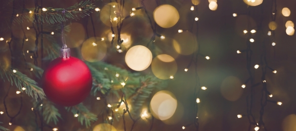 A red Christmas ornament hangs on a tree surrounded by strings of twinkle lights.