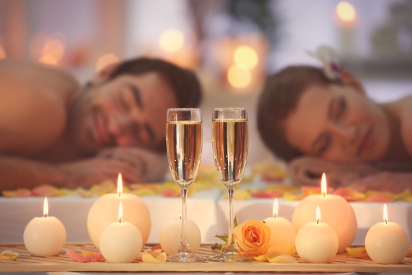 A man and a woman lie head to head in a serene setting with candles and glasses of Champagne.