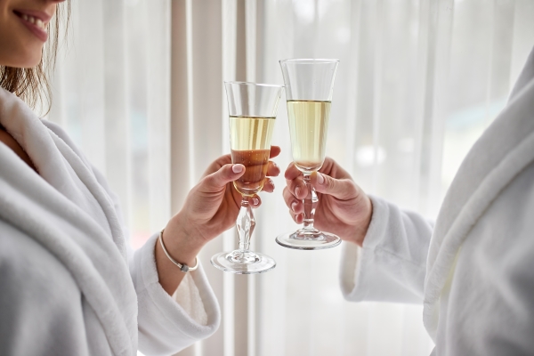 A close-up of a couple in matching white robes toast glasses of Champagne. 