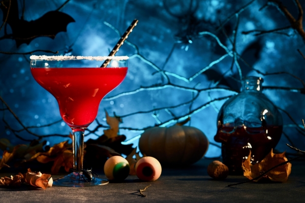 A blood red cocktail against a spooky backdrop with branches, bats, and eyeballs.
