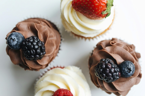 An overhead shot of four cupcakes, two with vanilla frosting and topped with strawberries and two with chocolate frosting topped with blackberries.