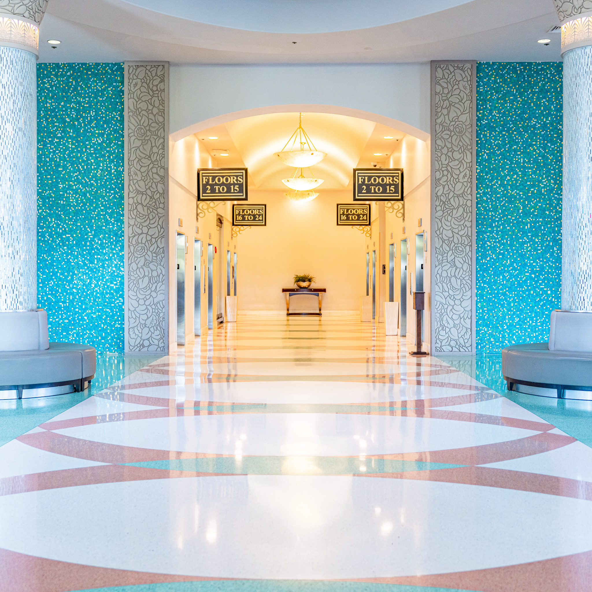 A grand tiled entryway with teal blue walls leading to a bay of elevators in the Rosen Centre lobby.