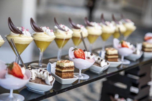 Two displayed rows of fancy desserts, including tiramisu, chocolate mousse, and a martini glass with custard and chocolate feather garnish.