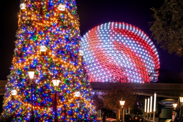 A colorfully lit Christmas tree stands in the foreground with a peppermint striped glowing Spaceship Earth in the background during the holidays at EPCOT.