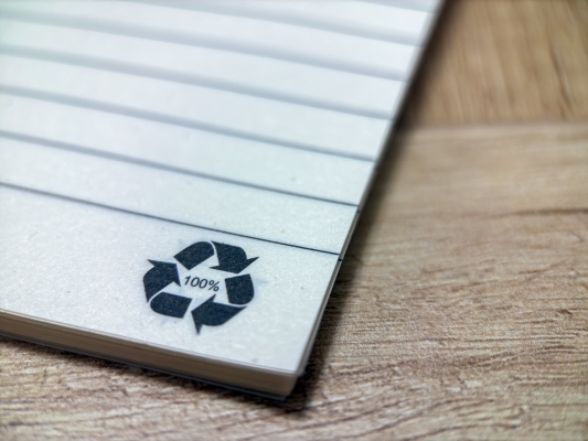 A close-up of a 100% recycled icon on the corner of a notepad.