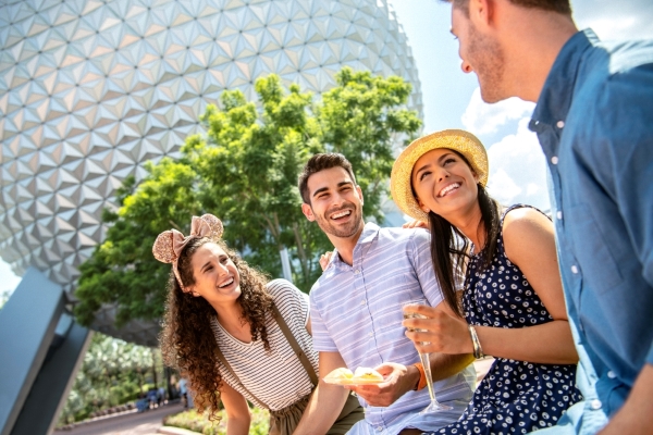 Four young adults smile at one another in front of Spaceship Earth at EPCOT while on a friendcation.