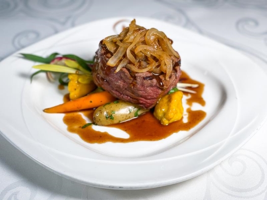 A filet topped with caramelized onions resting on a bed of carrots and jus.