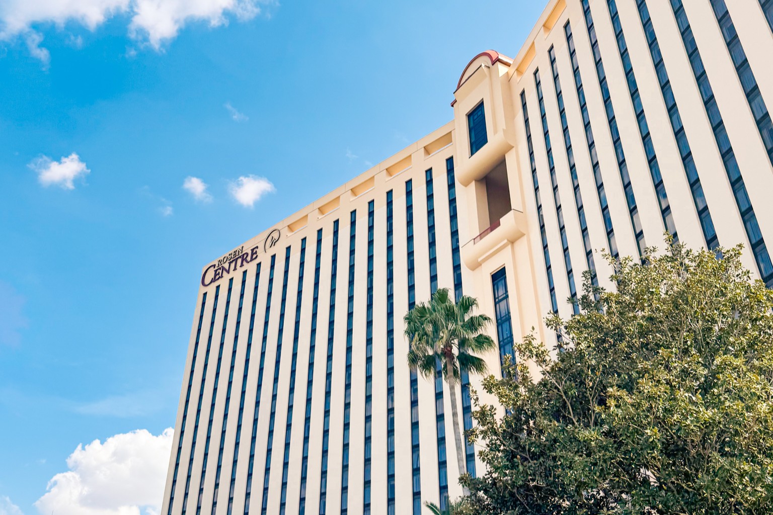 An upshot view of the exterior of Rosen Centre against a blue and cloudy sky. 