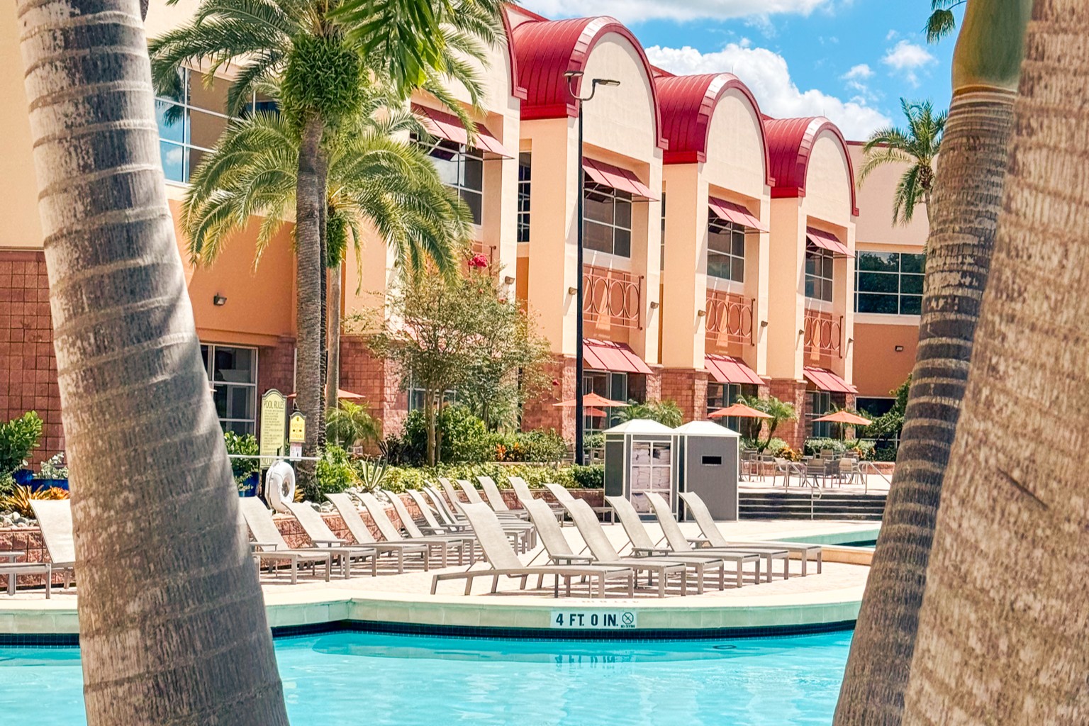 A row of arched windows with a red roof beside a row of white lounge chairs and a sparkling blue pool.