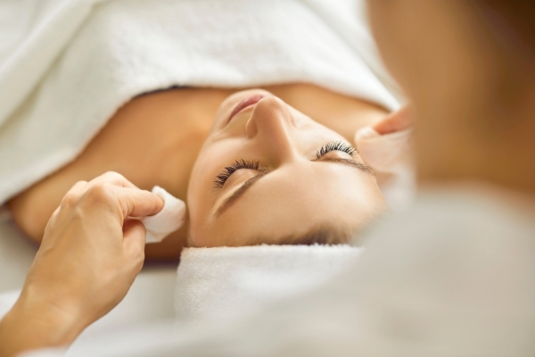 A woman wrapped in towels receives a facial treatment.