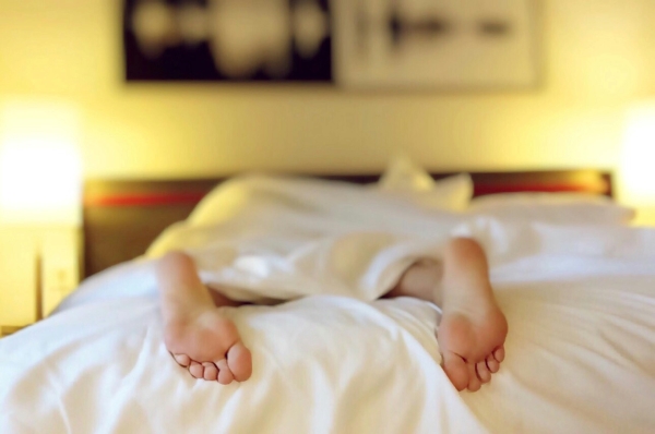 Two feet protruding from under white linens in a warmly lit bedroom.