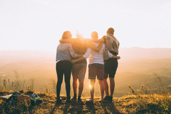 A group of four young adults hugging, silhouetted by the sunset.