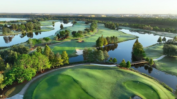 An aerial view of a sprawling golf course with trees, winding waterways, and clear sky.