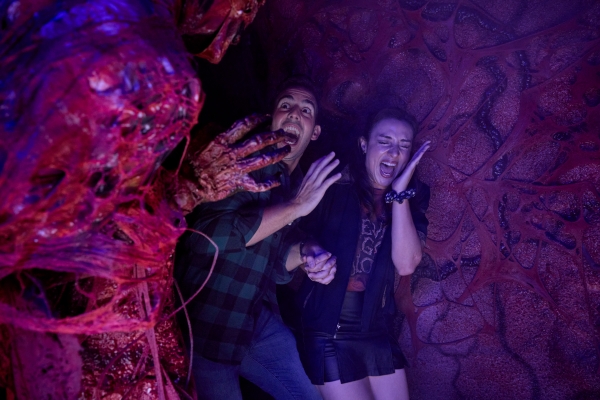 A man and woman scream in fear as they approach a gory, scary monster at HHN Orlando. 