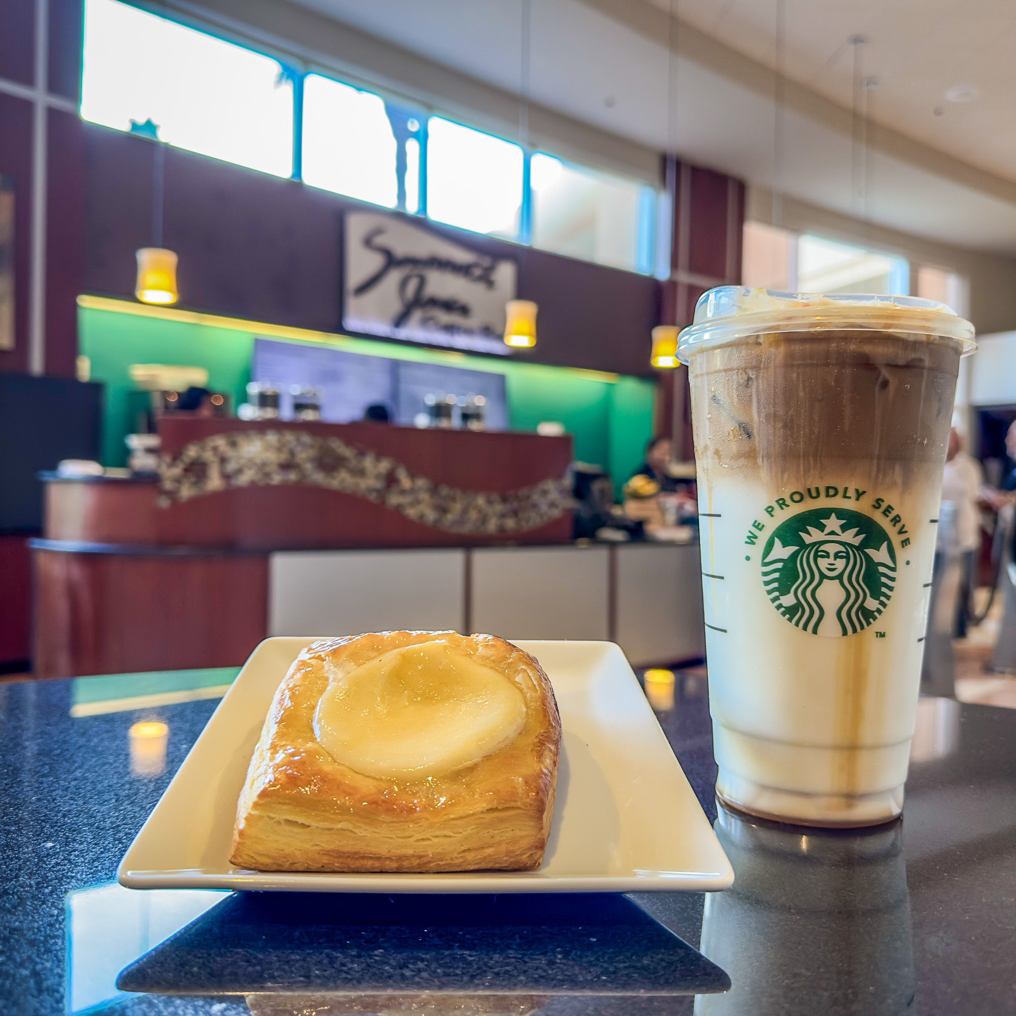 A pastry on a square white plate sits next to a coffee beverage in a Starbucks cup in front of Smoooth Java, a restaurant at Rosen Centre.