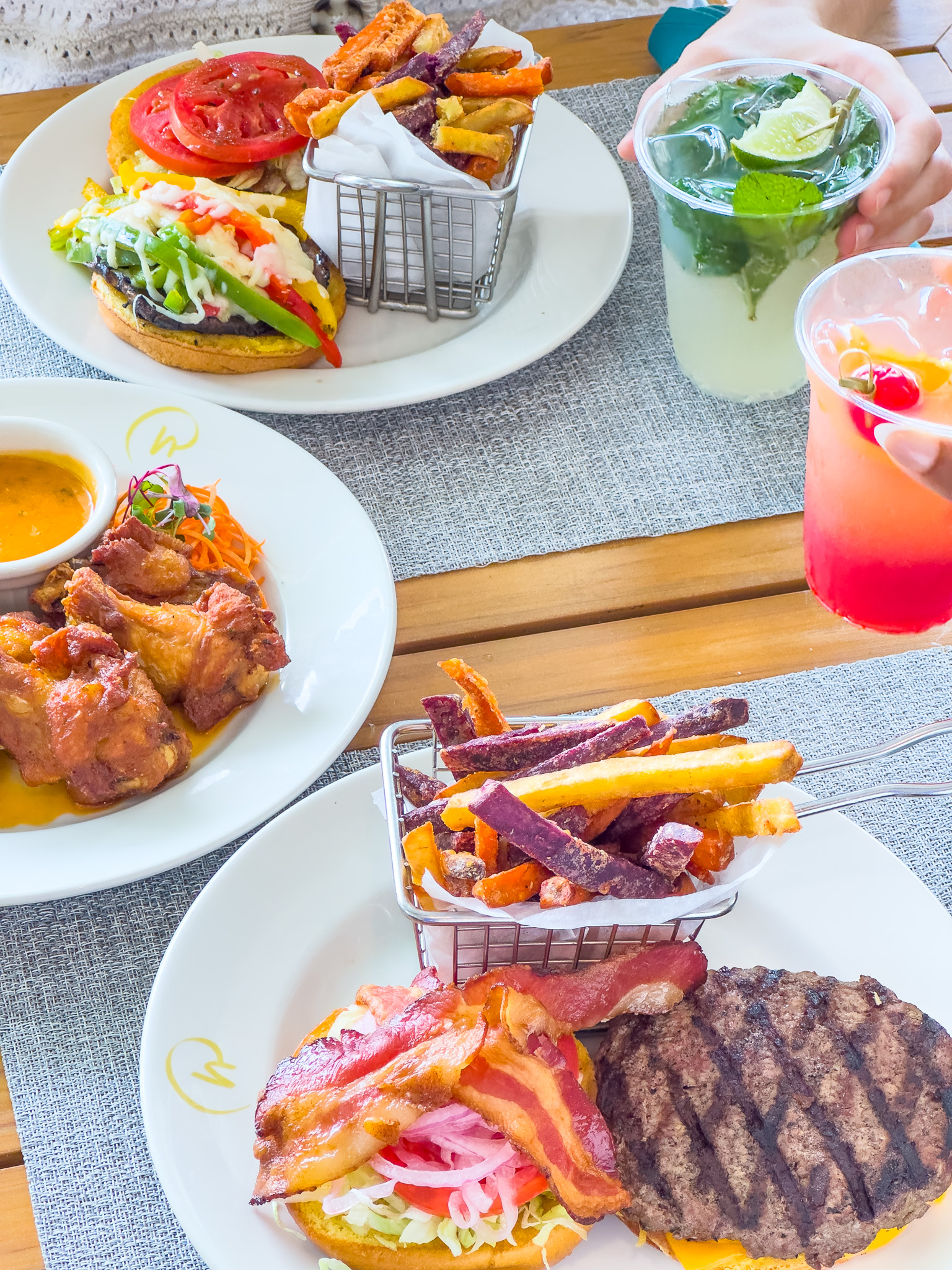 A tabletop array with plates of steak, chicken wings, cocktails, and other delicious food. 