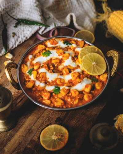 A metal bowl of a sauce-based Indian dish drizzled with a white sauce and garnished with slices of lemon.
