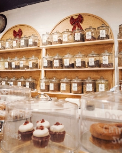 A cafe counter in front of decorative arched shelves displaying jars of loose leaf tea.