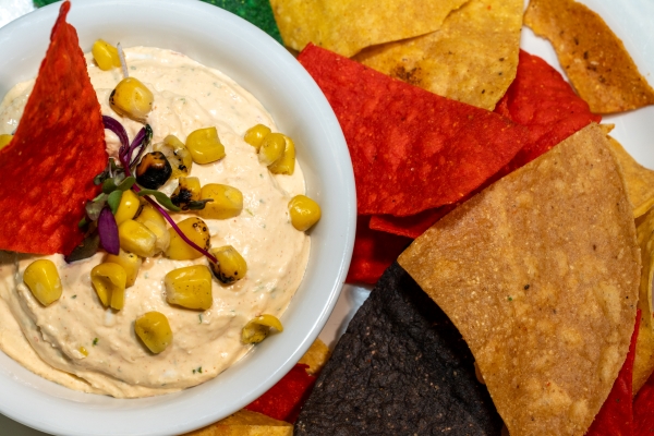 A close-up of a plate of tortilla chips and a cup of dip sprinkled with charred corn for Magical Dining 2026.