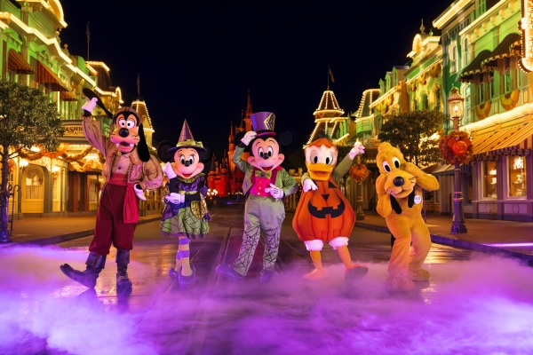 Goofy, Minnie, Mickey, Donald, and Pluto in Halloween costumes standing on Main Street at Night.