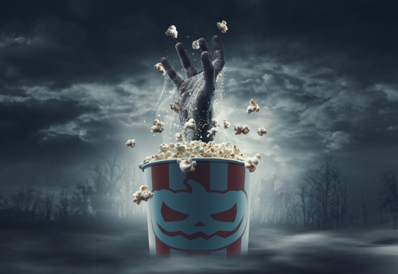 A gnarled monster hand emerges from a popcorn box with a creepy jack-o-lantern face.
