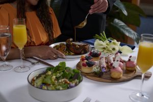 Rosen Centre Mother's Day table setting with salad, small desserts, orange juice, and a beef dish before a woman in an orange dress.