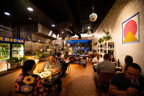 A dimly lit restaurant with tables of guests, an open kitchen, and disco balls hanging from the ceiling. Papa Llama, a Michelin Star restaurant in Orlando.