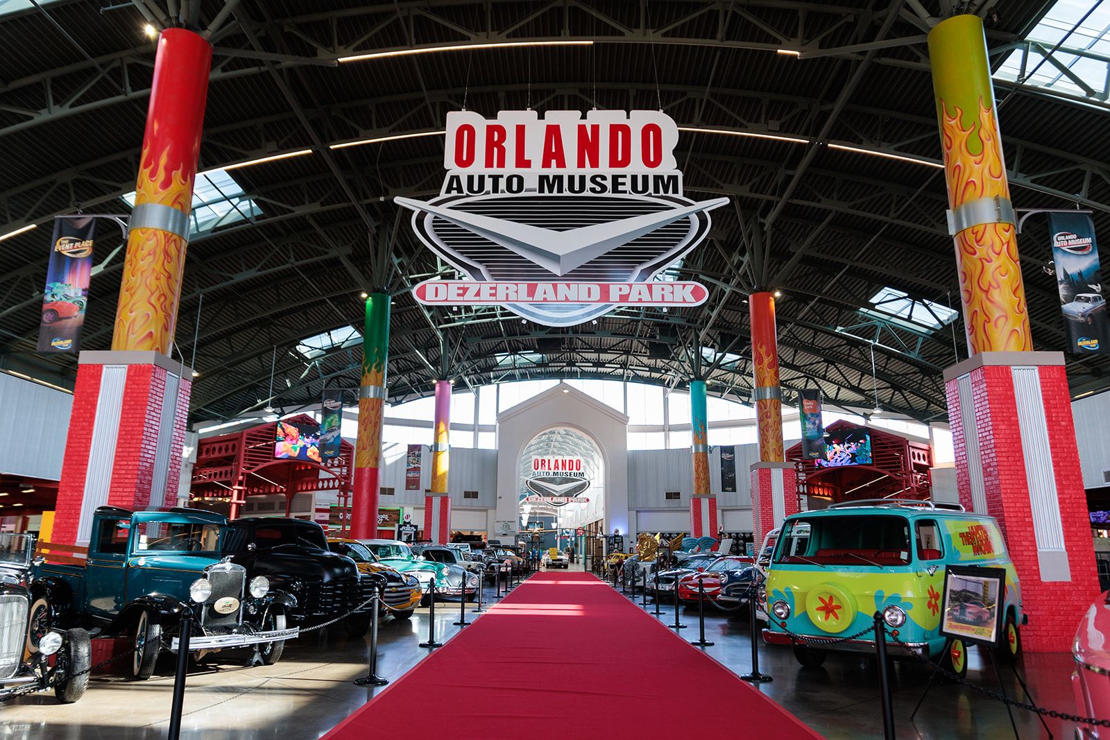 A long red carpet lined in classic cars under a hanging sign that reads Orlando Auto Museum