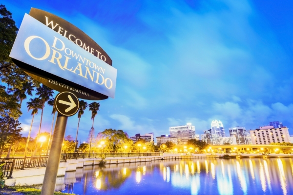 A sign that says Downtown Orlando at twilight, with a glowing skyline and a still lake behind.
