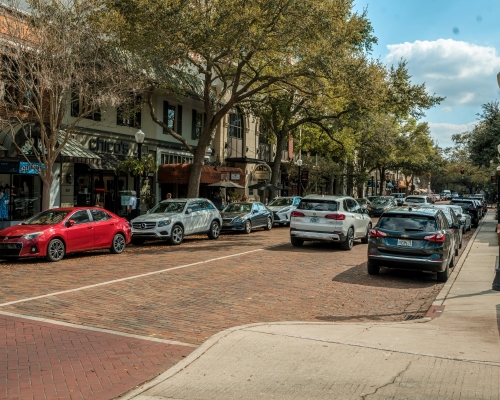 A cobblestone street lined with upscale stores and trees, with cars facing both directions.