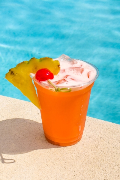 A bright orange cocktail with a cherry and pineapple garnish sits on a pool deck beside clear blue water at Rosen Centre in Orlando.