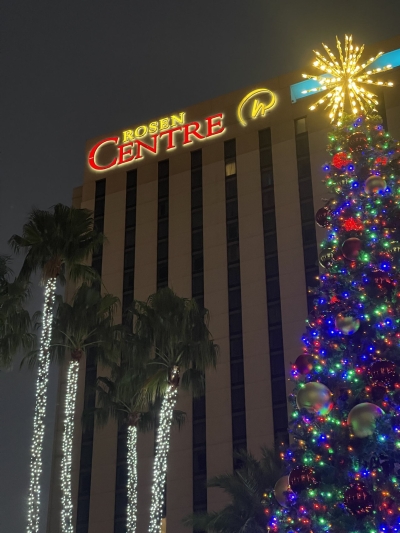 The exterior of Rosen Centre at night behind a tall Christmas tree and palm trees wrapped in Christmas lights. Stay here while celebrating theme park holidays.