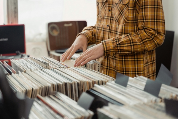 A close-up of a person in a yellow flannel shirt searching through rows of records for sale.