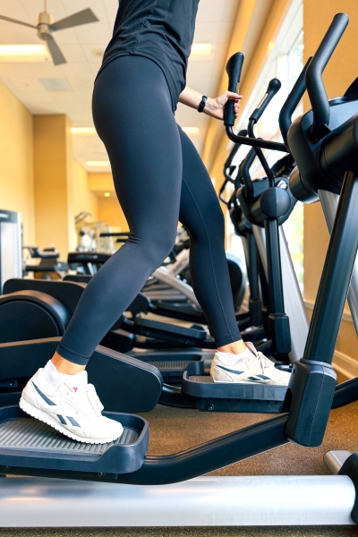A woman wearing black leggings and white sneakers exercises on an elliptical machine at the Rosen Centre fitness center. 