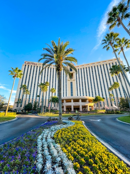 Flowers blooming and palm trees swaying underneath a bright blue sky at the entrance to Rosen Centre hotel on International Drive in Orlando.